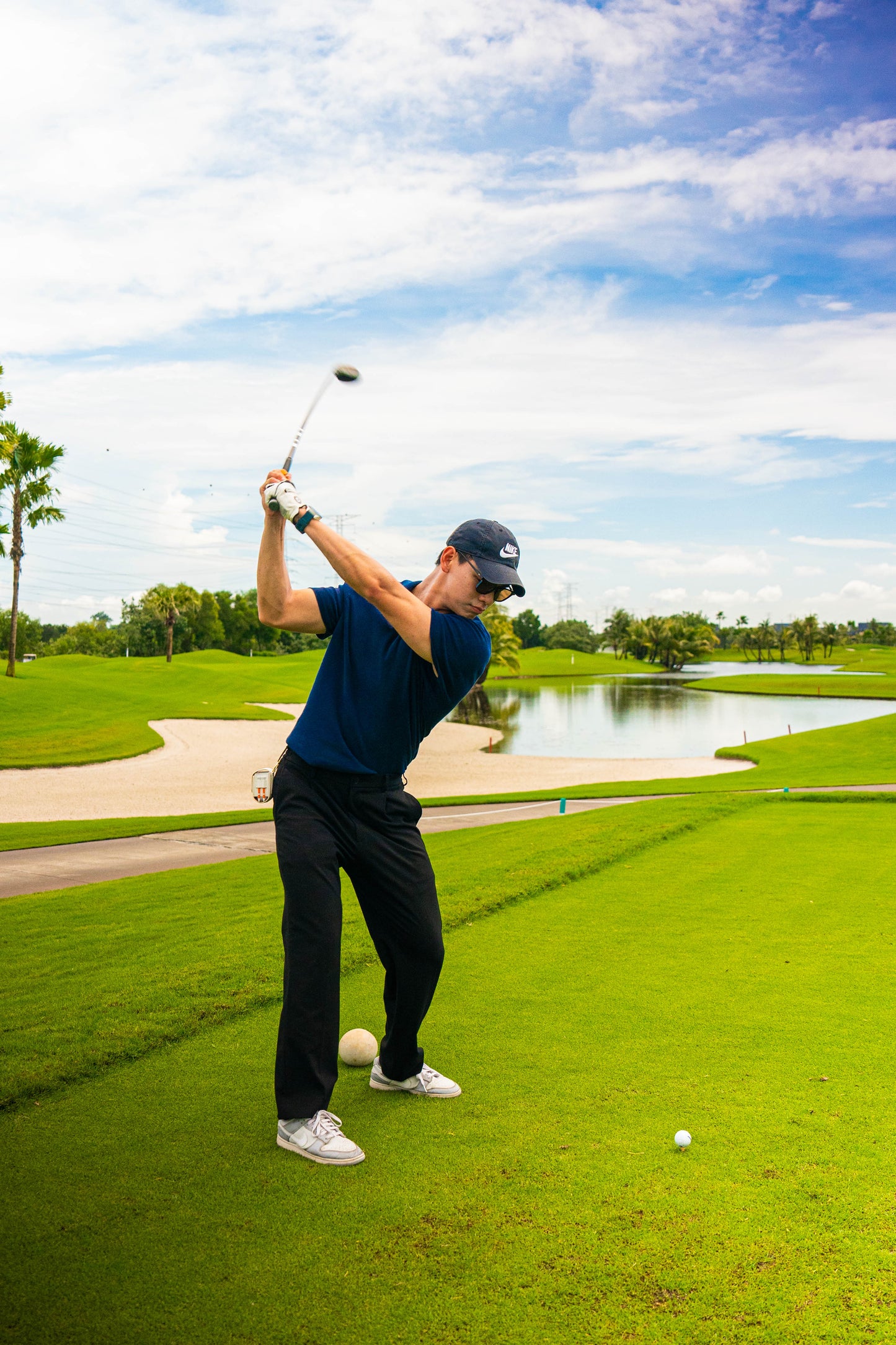 Male golfer swinging his golf clubs while wearing a white golf ball pouch.