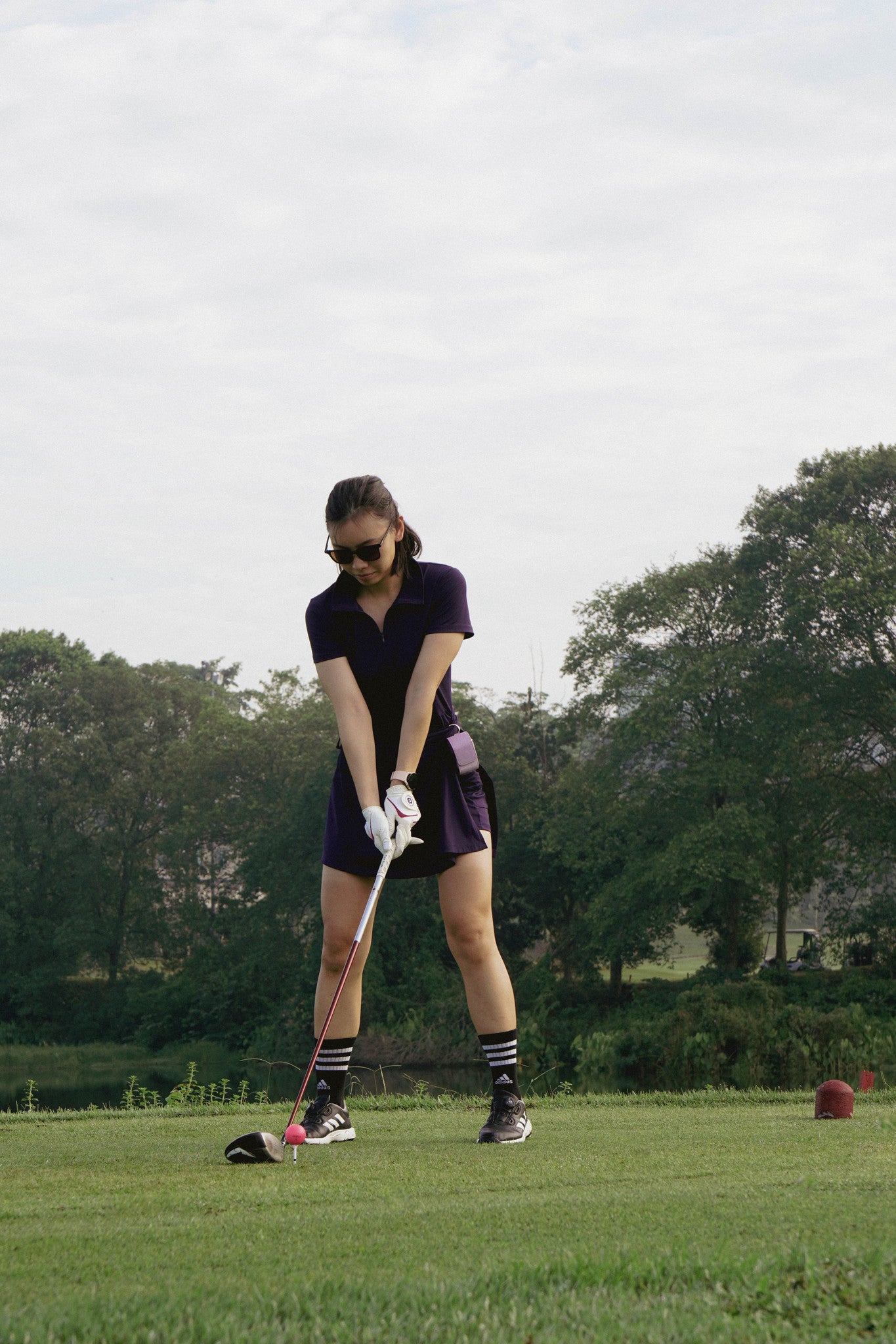 Female golfer on the tee box wearing paxton golf sunglasses and purple golf ball pouch