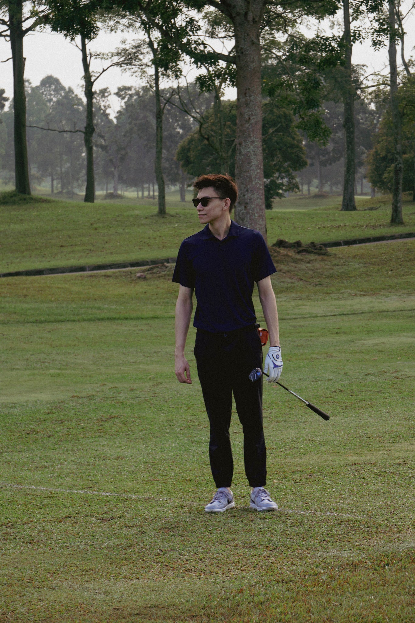 Male golfer on the golf course wearing paxton golf sunglasses an a orange golf ball pouch